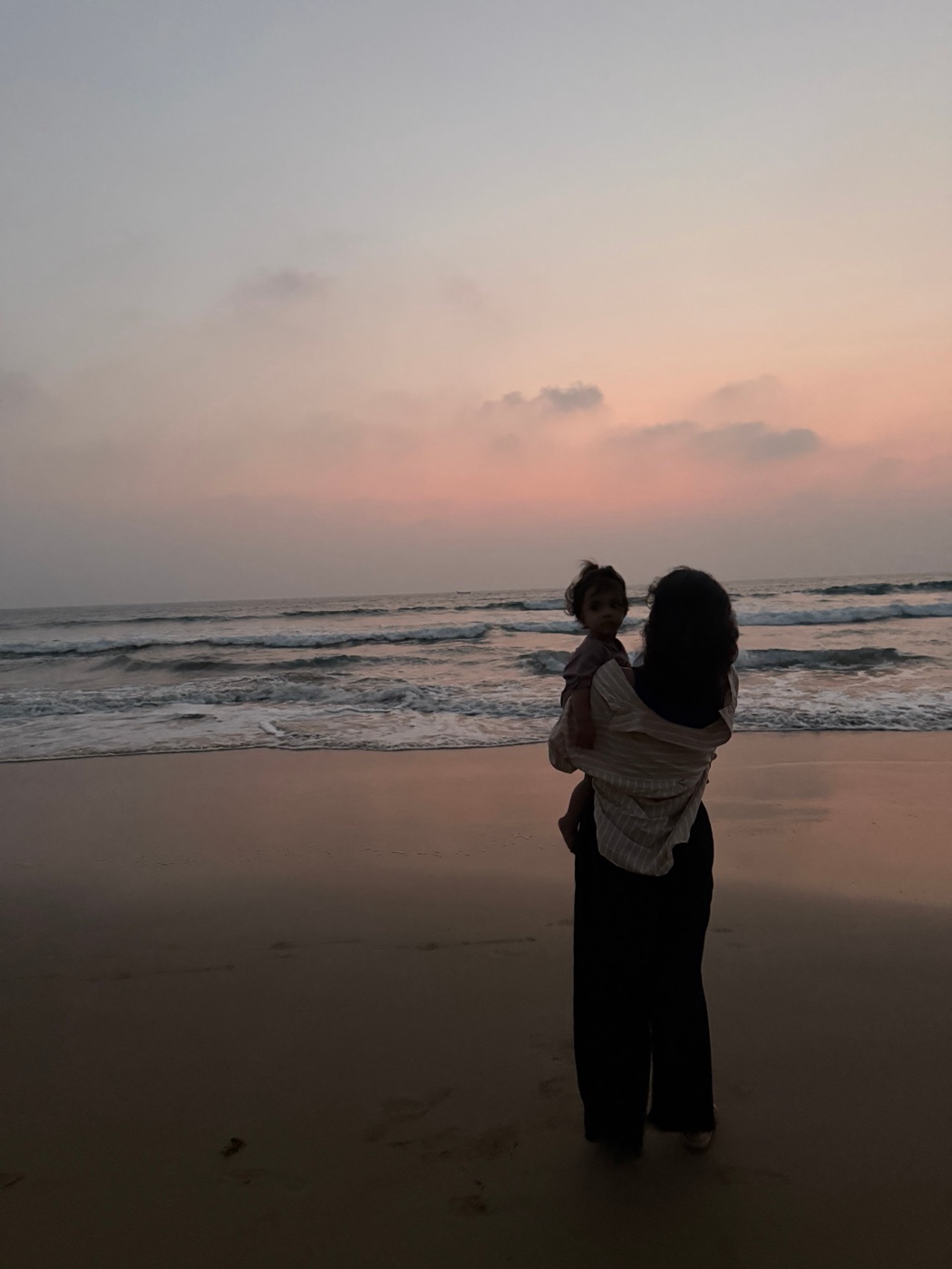 A mother holding her toddler on the beach at sunset